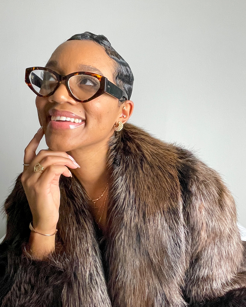 black woman in glasses smiling in a fur coat